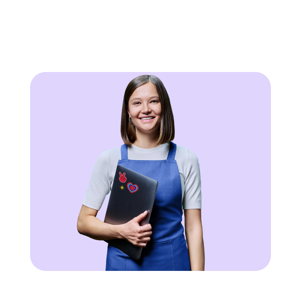 Smiling young woman in blue apron holding decorated laptop against purple background