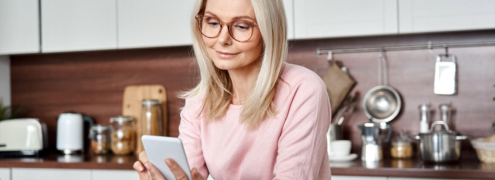 Woman in kitchen looking at cell phone in her hand