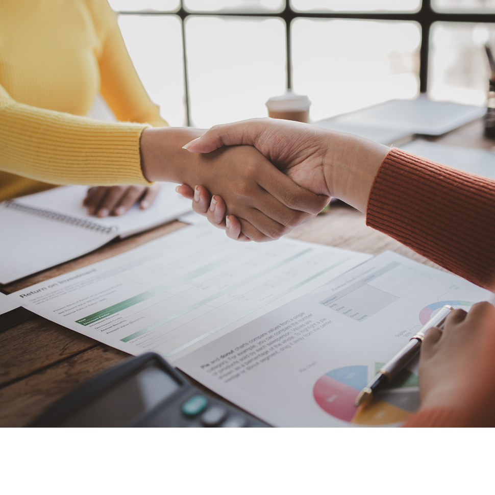 Two people shaking hands over financial documents