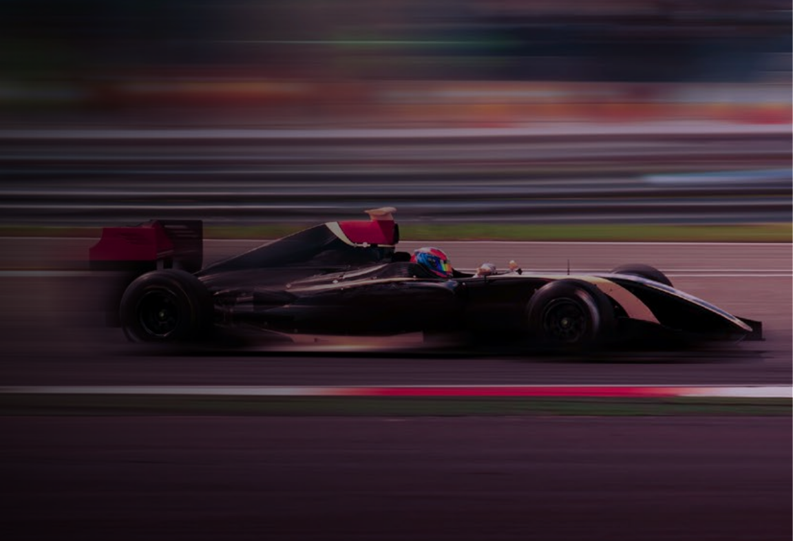 Formula 1 racing car speeding on track with motion blur effect, driver wearing colourful helmet.