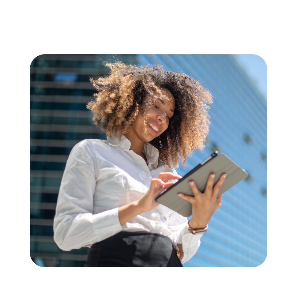 Woman with curly hair in white shirt holding tablet outdoors against blue sky and building